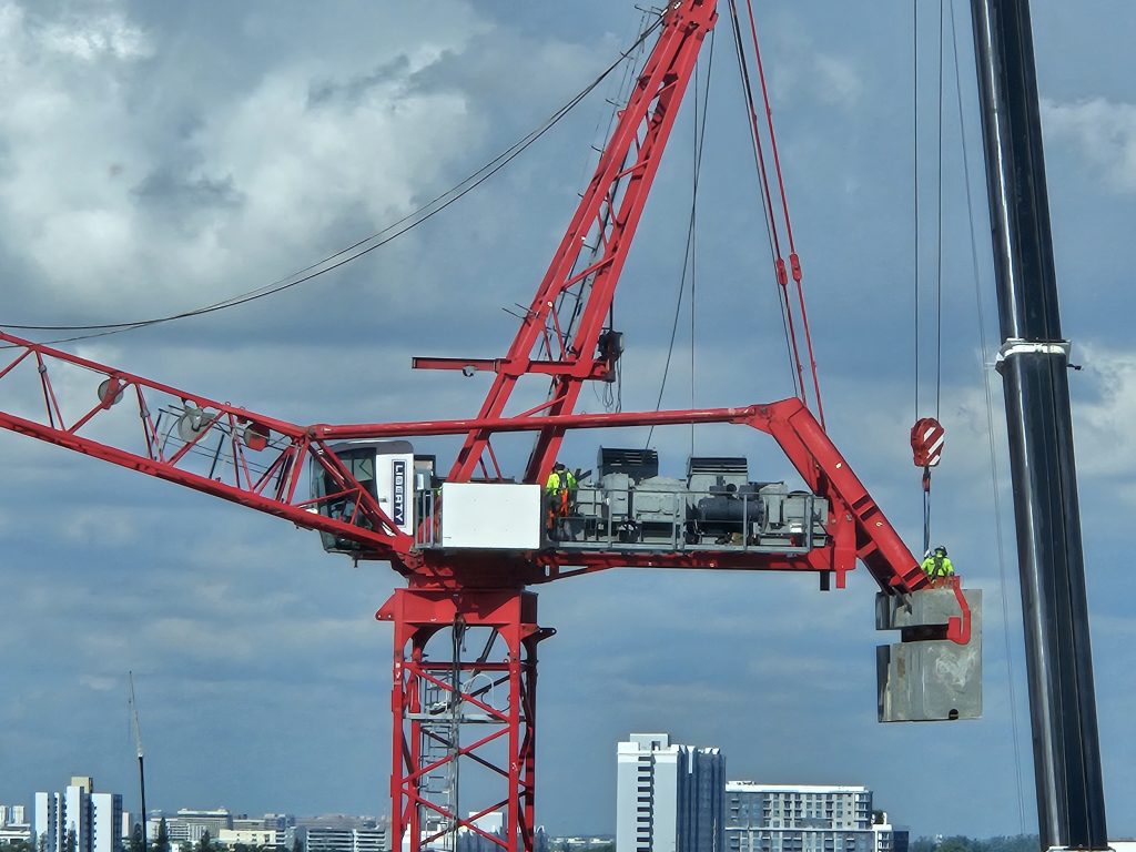 Red tower crane undergoing inspection with workers on-site, ensuring structural safety and compliance.